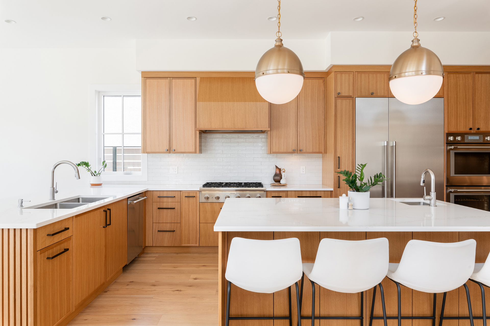 Warm white oak kitchen with brass globe pendants and a large quartz island